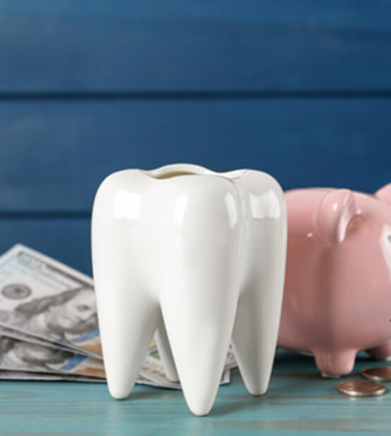 A ceramic model of a tooth, a piggy bank, and money on a blue wooden table